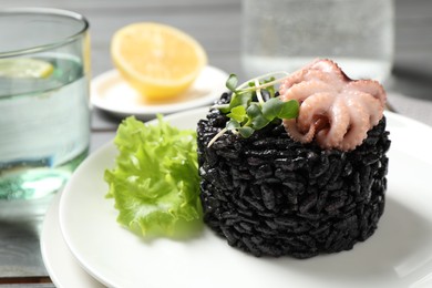 Photo of Delicious black risotto with baby octopus on table, closeup
