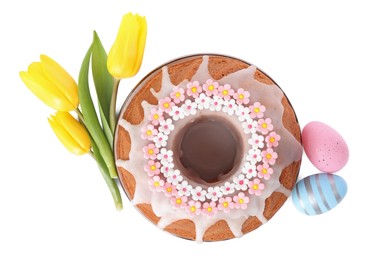 Photo of Festively decorated Easter cake, painted eggs and yellow tulips on white background, top view
