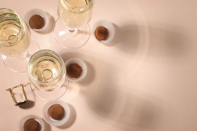Photo of Glasses of delicious sparkling wine and chocolate truffles on pale pink background, above view. Space for text