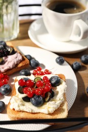 Cup of coffee near sandwiches with cream cheese and berries on wooden tray