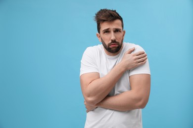 Man suffering from fever on light blue background, space for text. Cold symptoms