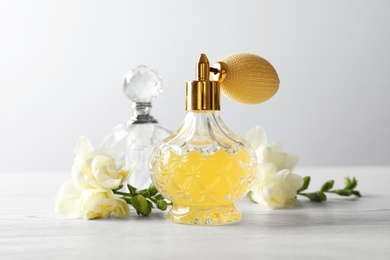Different perfume bottles and flowers on light background
