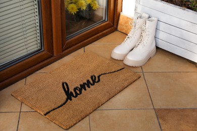 Photo of Doormat with word Home and stylish boots near entrance outdoors