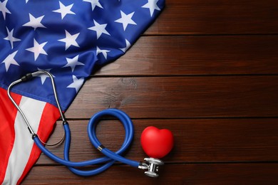 Stethoscope, red heart and American flag on wooden table, flat lay. Space for text