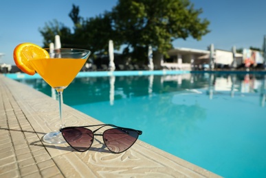Tasty refreshing cocktail and sunglasses on edge of swimming pool. Party items