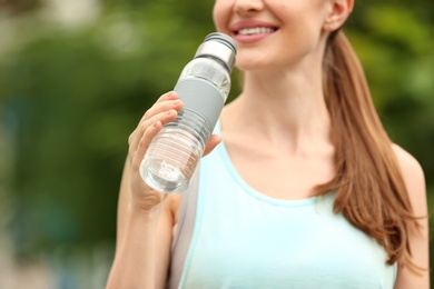 Young woman with bottle of water outdoors, closeup. Refreshing drink