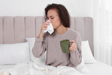 Sick African American woman with tissue and cup of drink in bed at home