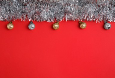 Silver tinsel and Christmas balls on red background, flat lay. Space for text
