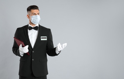 Waiter in medical face mask with menu on light grey background. Space for text
