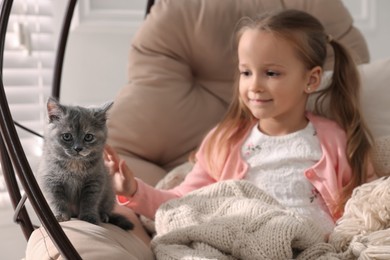 Cute little girl with kitten in hanging chair at home. Childhood pet