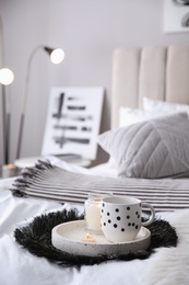 Cup of drink and burning candles on bed in room, space for text. Interior design