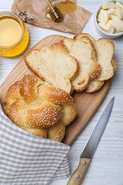 Cut freshly baked braided bread, honey and butter on white wooden table, flat lay. Traditional Shabbat challah