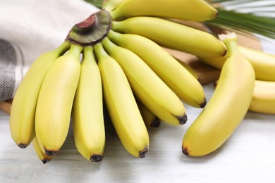Tasty ripe baby bananas on white wooden table, closeup