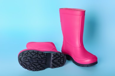 Pair of bright pink rubber boots on light blue background