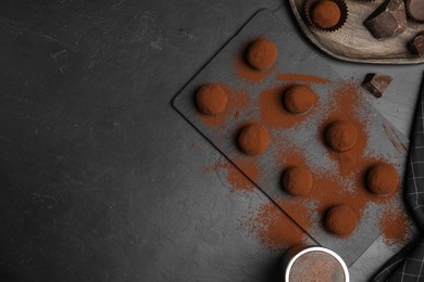 Delicious chocolate truffles powdered with cocoa on black table, flat lay. Space for text