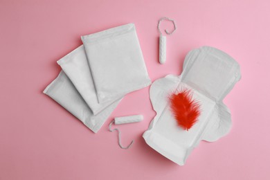 Menstrual pads, tampons and feather on pink background, flat lay