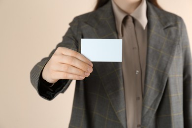 Woman holding white business card on beige background, closeup