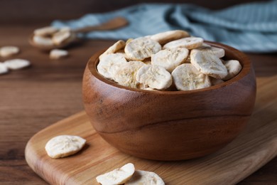 Photo of Bowl and dried banana slices on wooden table, closeup