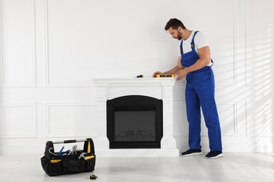 Professional technician using construction level for installing electric fireplace in room