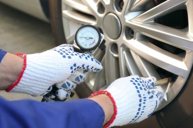 Mechanic checking air pressure in car tire outdoors, closeup