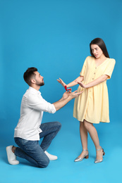 Young woman rejecting engagement ring from boyfriend on blue background