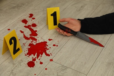Crime scene markers and dead body with bloody knife on floor, closeup