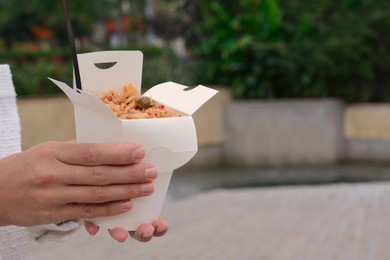 Woman holding paper box of takeaway noodles with fork outdoors, closeup and space for text. Street food