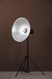 Professional beauty dish reflector on tripod near brown wall in room. Photography equipment
