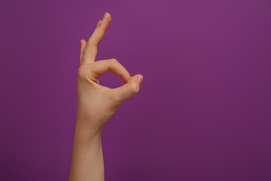 Woman showing okay gesture on purple background, closeup. Space for text