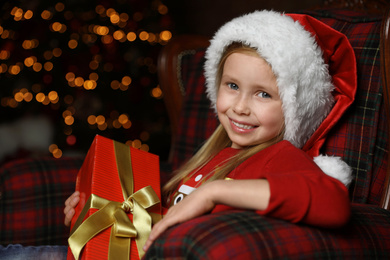 Photo of Cute little child with Christmas gift sitting in armchair at home