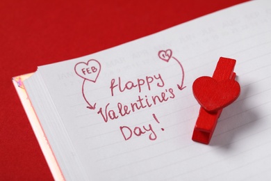 Notebook with text Happy Valentine's Day! and clothespin on red background, closeup
