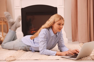 Photo of Young woman working on laptop near fireplace in room