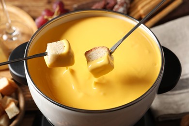 Dipping pieces of bread into tasty cheese fondue, closeup