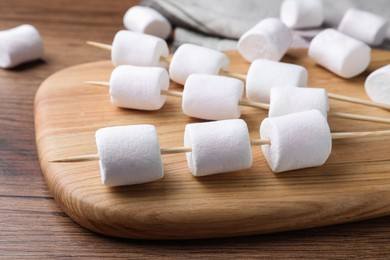 Sticks with delicious puffy marshmallows on wooden table, closeup