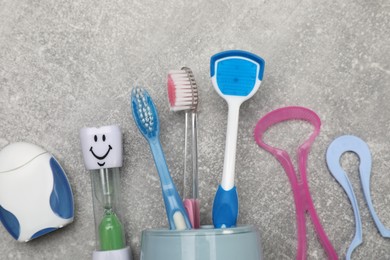Tongue cleaners, toothbrushes, dental floss and hourglass on light grey background, flat lay