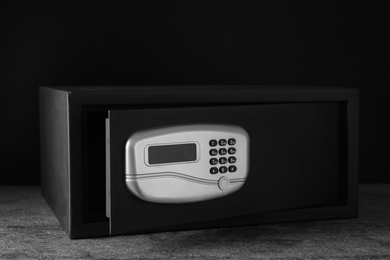 Black steel safe with electronic lock on grey table against dark background