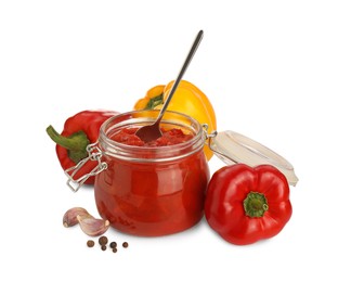 Photo of Glass jar of delicious canned lecho, fresh vegetables and peppercorns on white background
