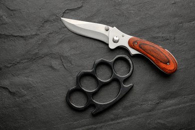 Brass knuckles and knife on black background, flat lay