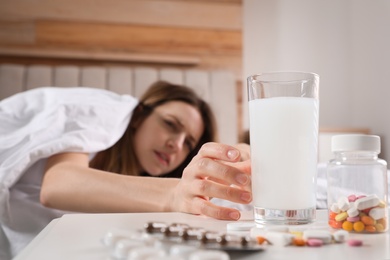 Woman taking medicine for hangover in bed at home, focus on hand with glass