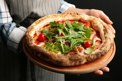 Woman holding tasty pizza with meat and arugula on black background, closeup