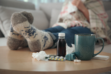 Person in warm socks near table with different remedies indoors, closeup. Influenza virus