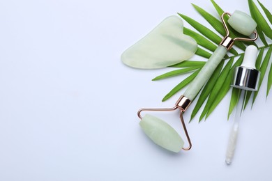 Gua sha stone, face roller, dropper and green leaves on white background, flat lay. Space for text