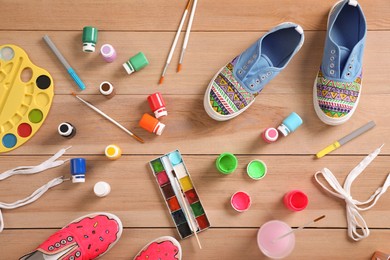 Sneakers and painting supplies on wooden table, flat lay. Customized shoes