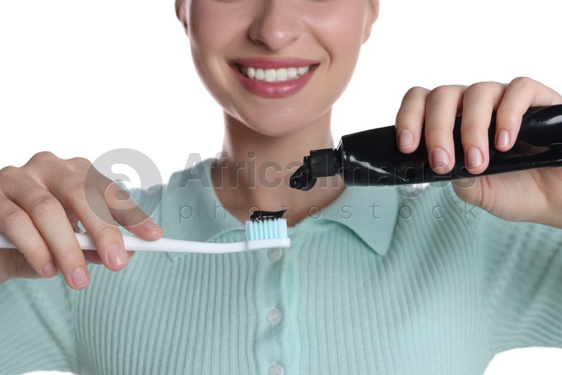 Woman applying charcoal toothpaste onto brush on white background, closeup