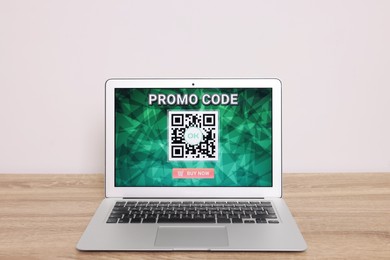 Photo of Laptop with activated promo code on wooden table near white wall