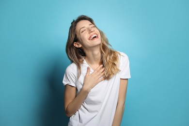 Cheerful young woman laughing on light blue background
