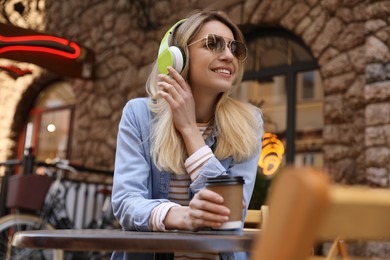 Happy young woman with coffee and headphones listening to music in outdoor cafe
