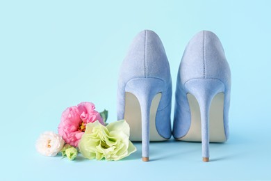 Stylish women's high heeled shoes and beautiful flowers on light blue background