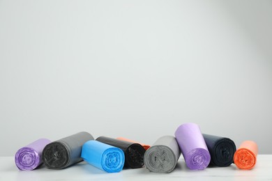 Photo of Rolls of different color garbage bags on table against light background. Space for text