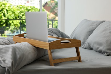 Wooden tray table with laptop on bed indoors